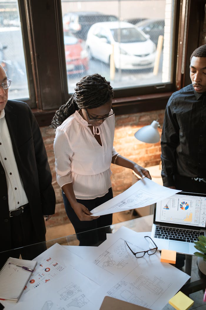 A diverse business team reviews printed plans in a modern office setting.